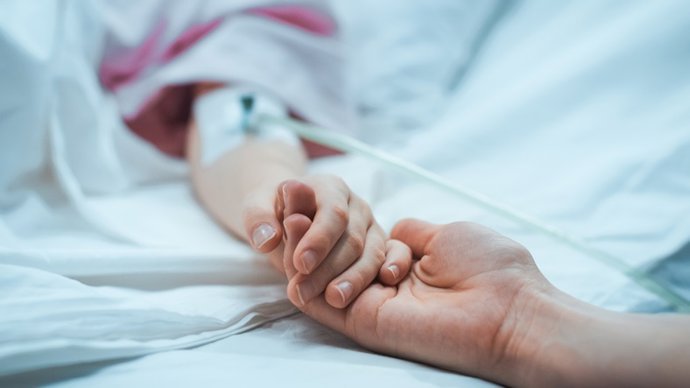 Archivo - Recuperaci&oacute;n ni&ntilde;o peque&ntilde;o acostado en la cama del Hospital para dormir, la madre sostiene su mano reconfortante. Se centran en las manos. Emotivo momento familiar.